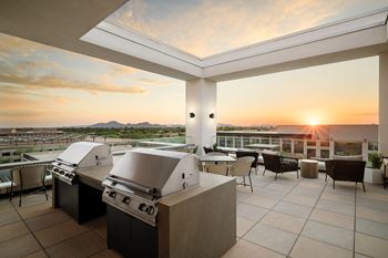 A modern outdoor kitchen with a grill and seating area overlooking a sunset.